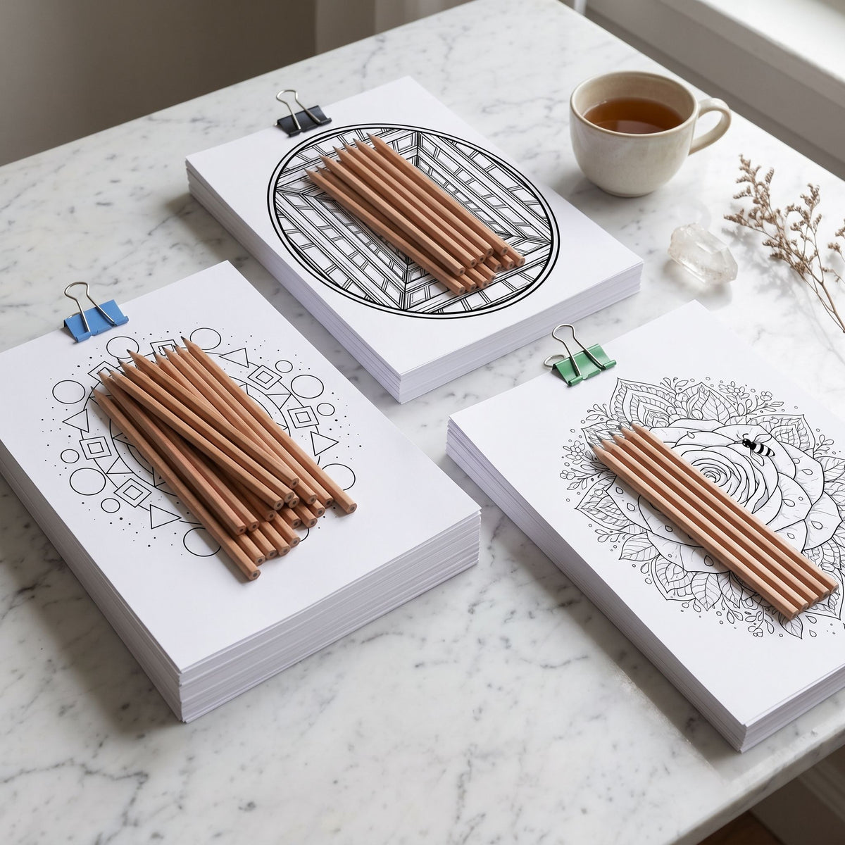 Trío Mente en Blanco, combo de mandalas Geométricos, Flores & Naturaleza e Hipnóticos para colorear, vista en ángulo sobre mármol blanco con lápices, taza y cuarzo - Calma en Tinta