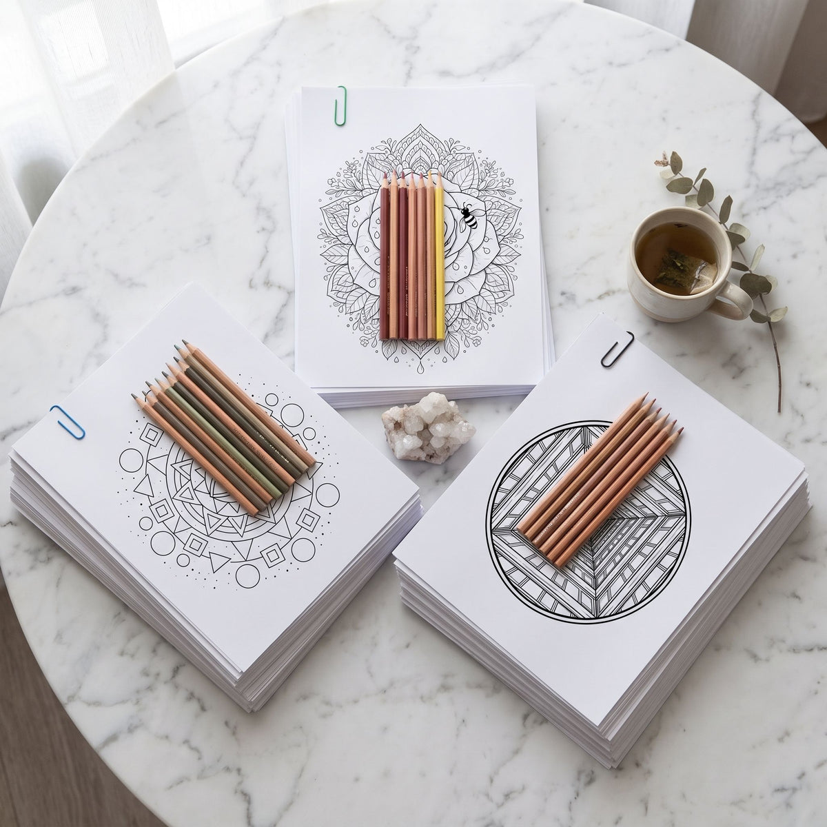 Trío Mente en Blanco, combo de mandalas Geométricos, Flores & Naturaleza e Hipnóticos para colorear, flat lay sobre mármol blanco con lápices, taza y cuarzo - Calma en Tinta